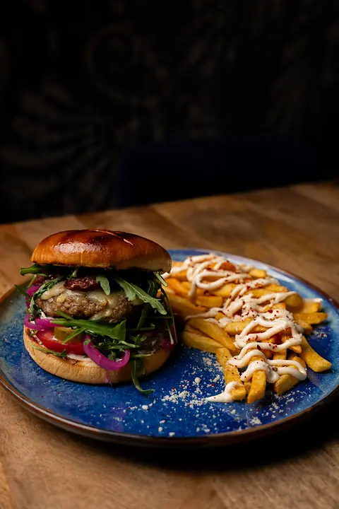Baku Lounge Burger z rukolą i marynowaną cebulą, obok frytki z sosem.