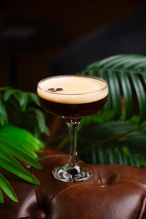Espresso martini z pianką i ziarnami kawy na skórzanym fotelu.