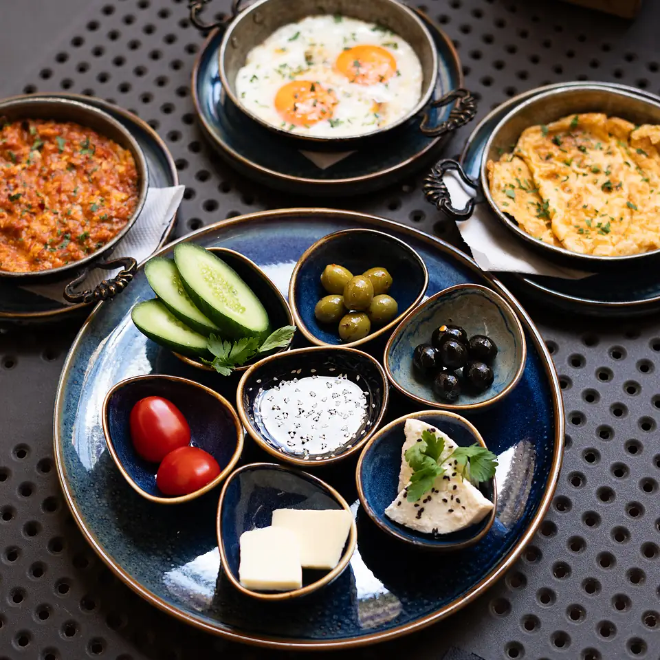 Śniadanie tureckie z góry: oliwki, ogórek, pomidory, ser feta i masło w miseczkach, obok jajka sadzone, omlet i menemen.